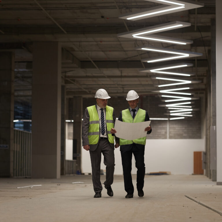 Image of project design team members reviewing drawings in a building under construction. Construction site shows part of lighting design solution installed.