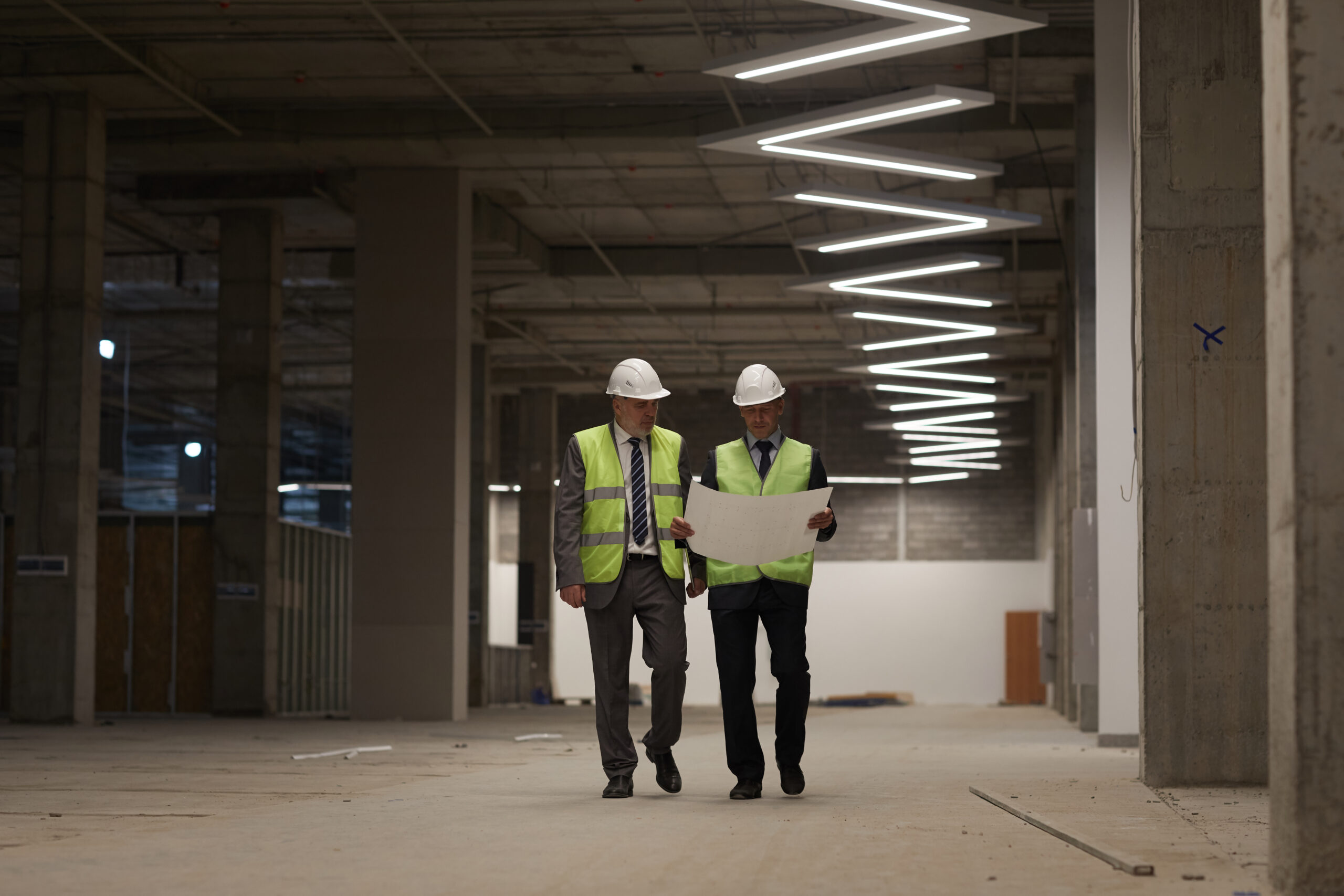 Image of project design team members reviewing drawings in a building under construction. Construction site shows part of lighting design solution installed.